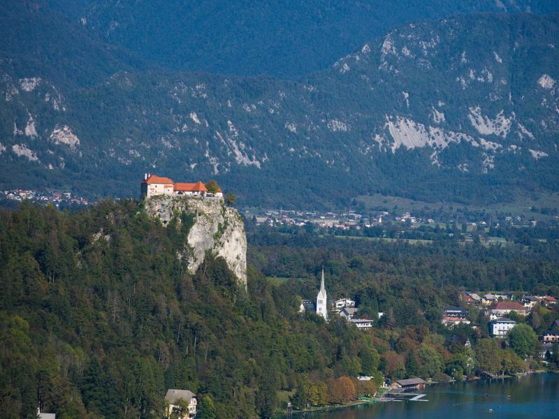 A stunning vertical shot of Bled Castle atop a cliff by Lake Bled with the Julian Alps in Slovenia.