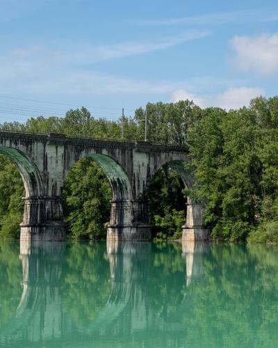 Beautiful arched railway bridge spanning across a serene river in Gorica, Radovljica, Slovenia, surrounded by lush greenery.