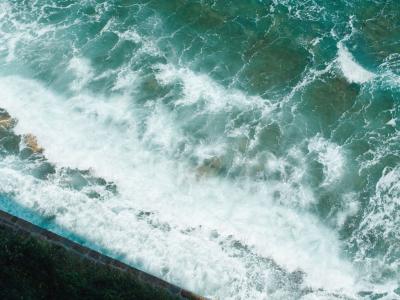 Beautiful aerial view of turquoise sea waves crashing on the rocky shore of Piran, Slovenia.