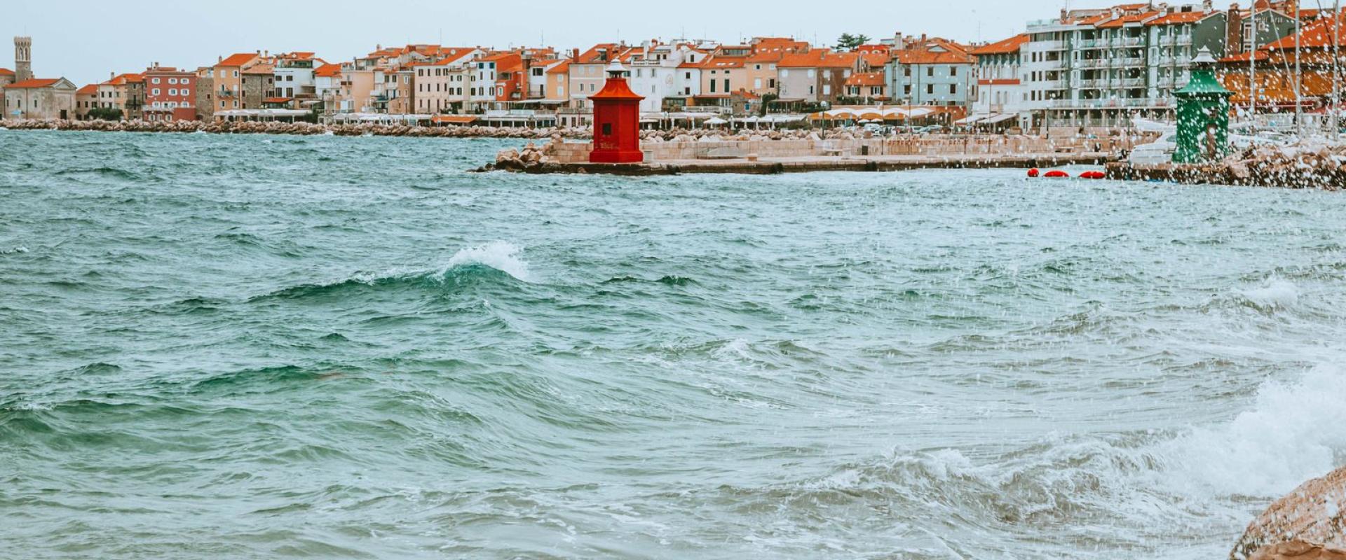 Picturesque coastal town of Piran, Slovenia, featuring vibrant houses and a red lighthouse by the Adriatic Sea.